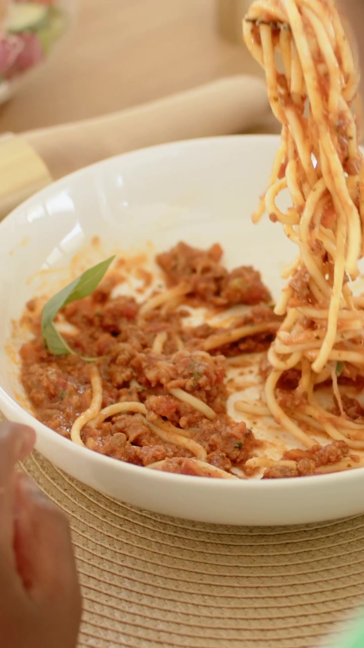 Video verticale: Commensale che preme una forchetta nera, avvolgendo gli spaghetti dalla ciotola, mangiando al tavolo, con basilico.