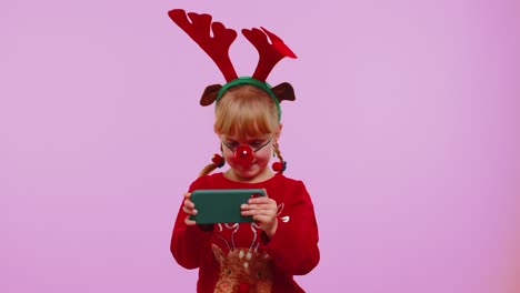 worried girl in christmas deer antlers enthusiastically playing racing video games on mobile phone