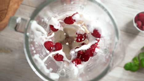batido de yogur cremoso de frambuesa mezclado en una licuadora de vidrio a cámara lenta, vista de arriba, dentro del dispositivo