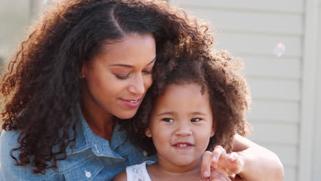 Mixed-race-mother-and-daughter-blowing-bubbles,-close-up