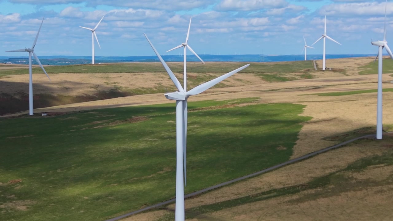 Ripresa aerea lenta in avvicinamento verso le turbine eoliche sparse in un paesaggio naturale. Clip aerea con drone di infrastrutture per la generazione di energia rinnovabile nel Regno Unito. 4K