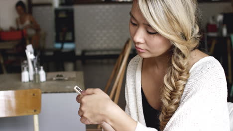 Mujer-Asiática-Comprando-Un-Teléfono-Inteligente-En-Línea-En-Una-Cafetería-Tomando-Café