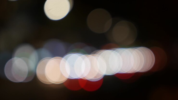 Beautiful glittering bokeh in dark blurry background at night. The round colorful bokeh shine from car lights on city street. Out of focus with blurry. Unfocused city lights. Traffic bokeh. Abstract concept