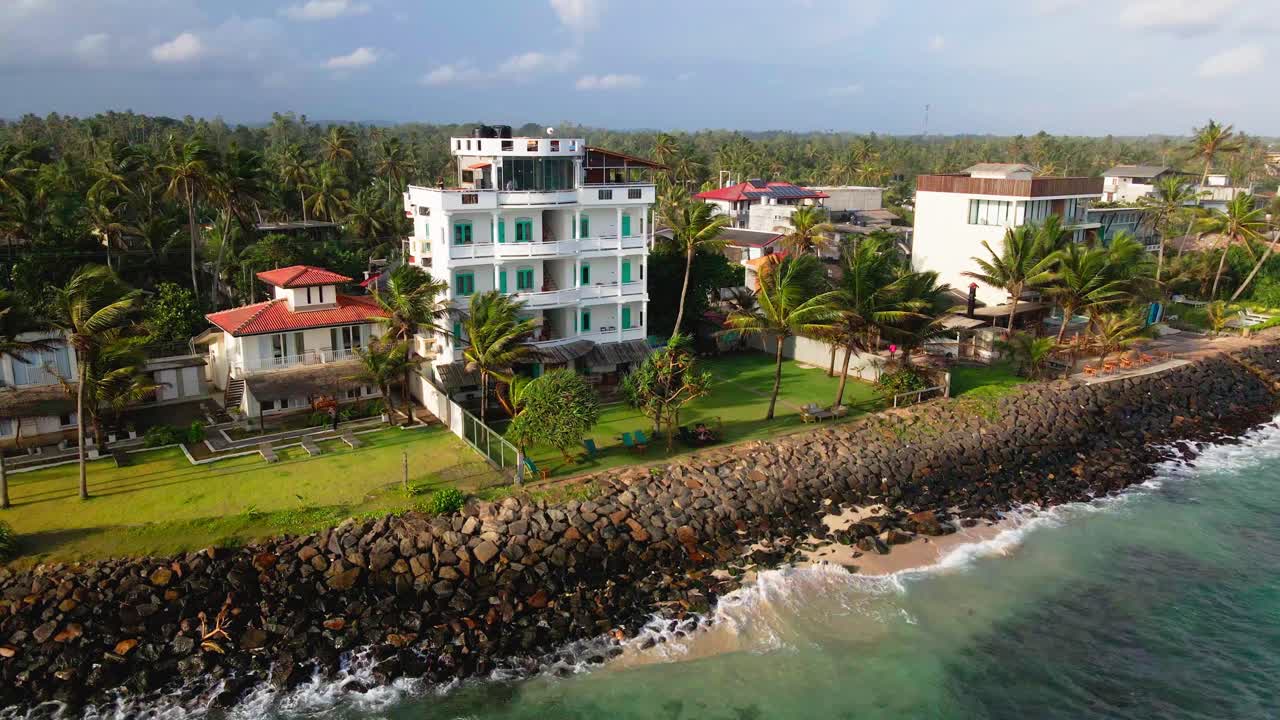 Aerial view of a coastal hotel by the ocean in Ahangama, Sri Lanka, featuring palm trees, a rocky shore, and surrounding buildings.