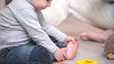 close up view of a baby sitting on the floor playing with building blocks and his mother holding his hands