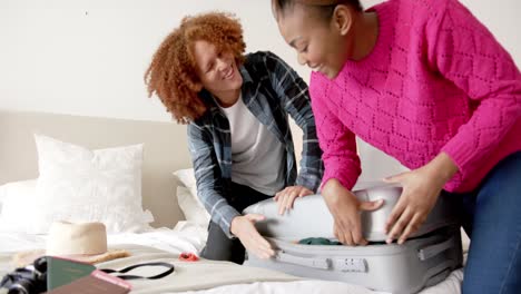 happy diverse couple packing and closing suitcase together in bedroom, slow motion