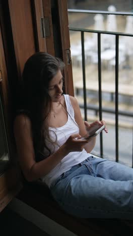 woman sitting by the window using phone