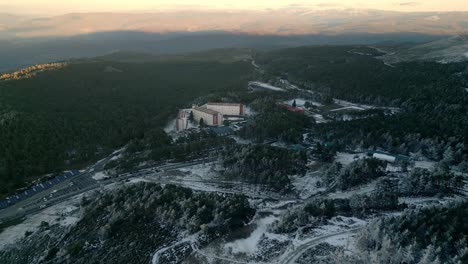 Aerial-shot-flying-over-a-snowy-forest-with-paths-and-highways-and-some-buildings-in-a-mountain-pass-in-Manzaneda,-Galicia