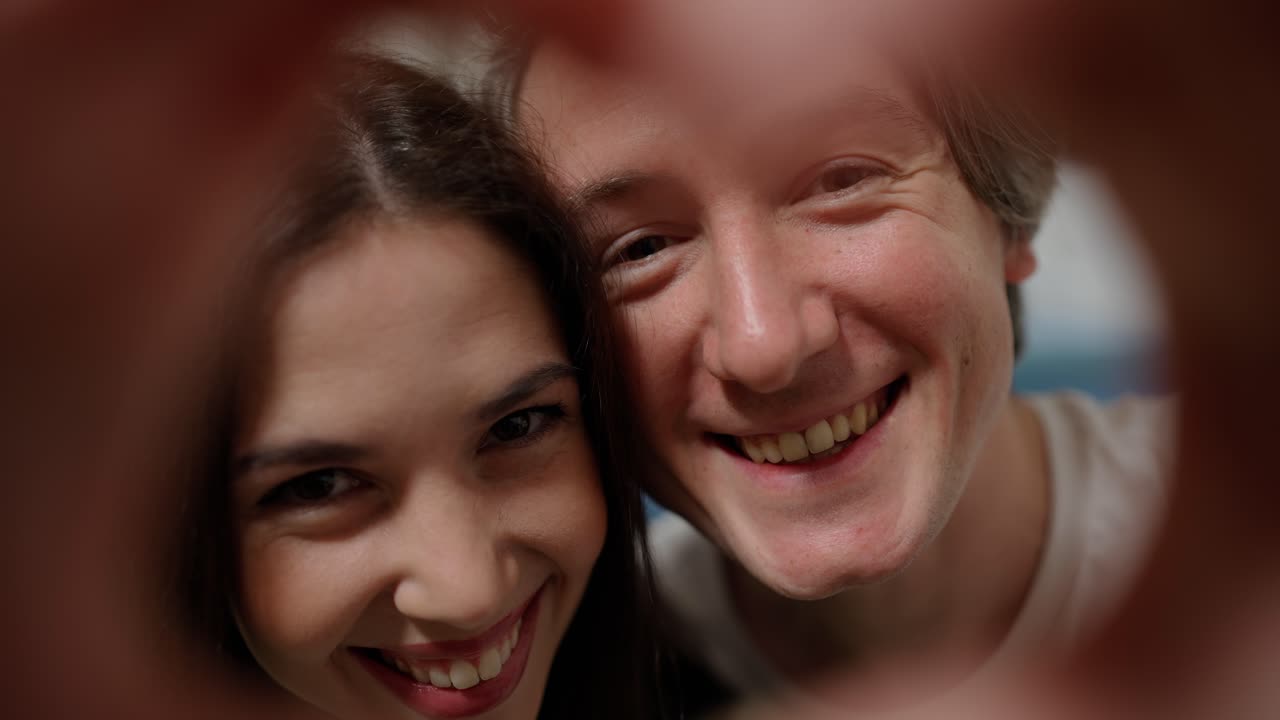 커플 얼굴이 손가락을  ⁇ 어서 심장 모양을 하고 있습니다.