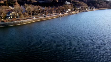 lakeside town during sunset with trees casting long shadows, aerial view