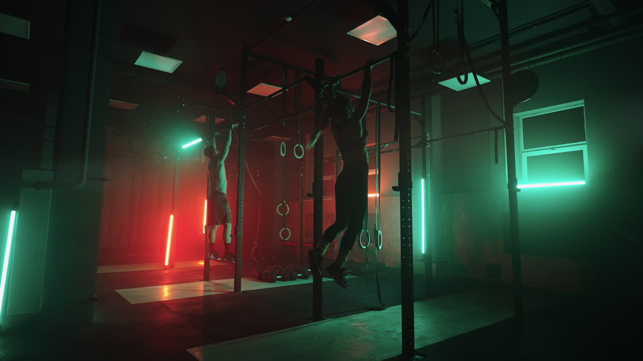 два мужчины и женщина в тренажерном зале делают подтягивания на горизонтальной стойке вместе в темном неоновом свете. атмосфера фитнеса и тренировки