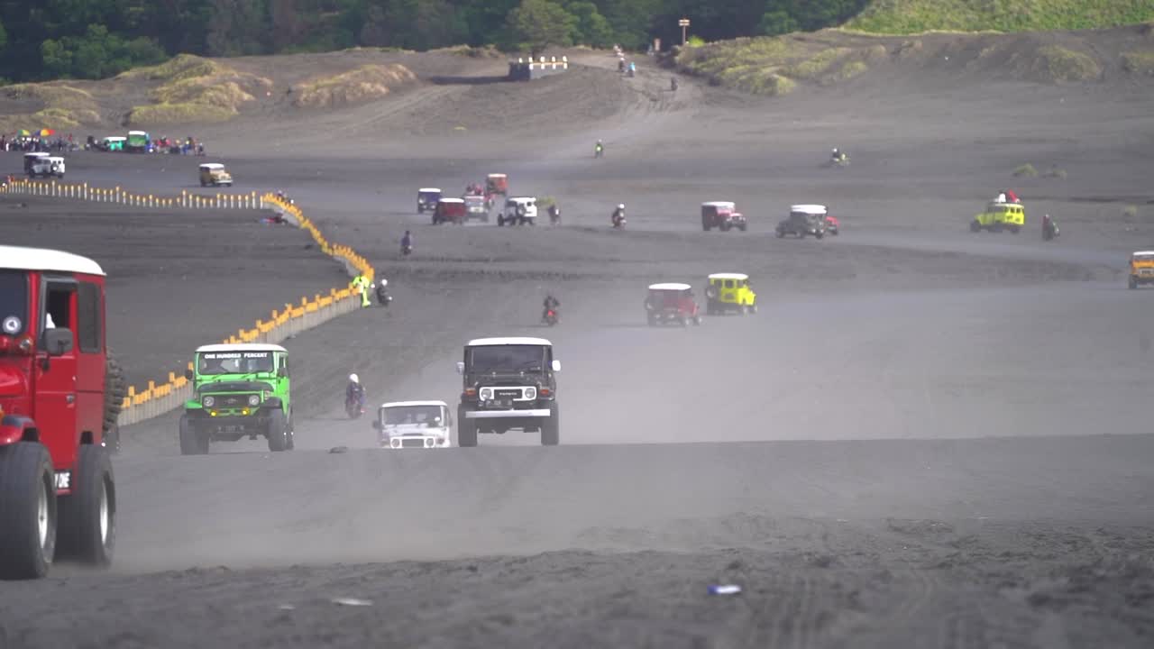 Slow motion shot of several Toyota Land Cruiser and motorcycles driving in the Sea of Sand at Mount Bromo, East Java, Indonesia