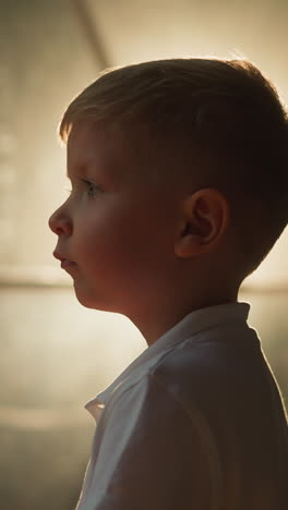 upset child stands near illuminated transparent wall of tent. tired boy inspects premise for tourists in evening closeup side view. rest in glamping area on blurred background