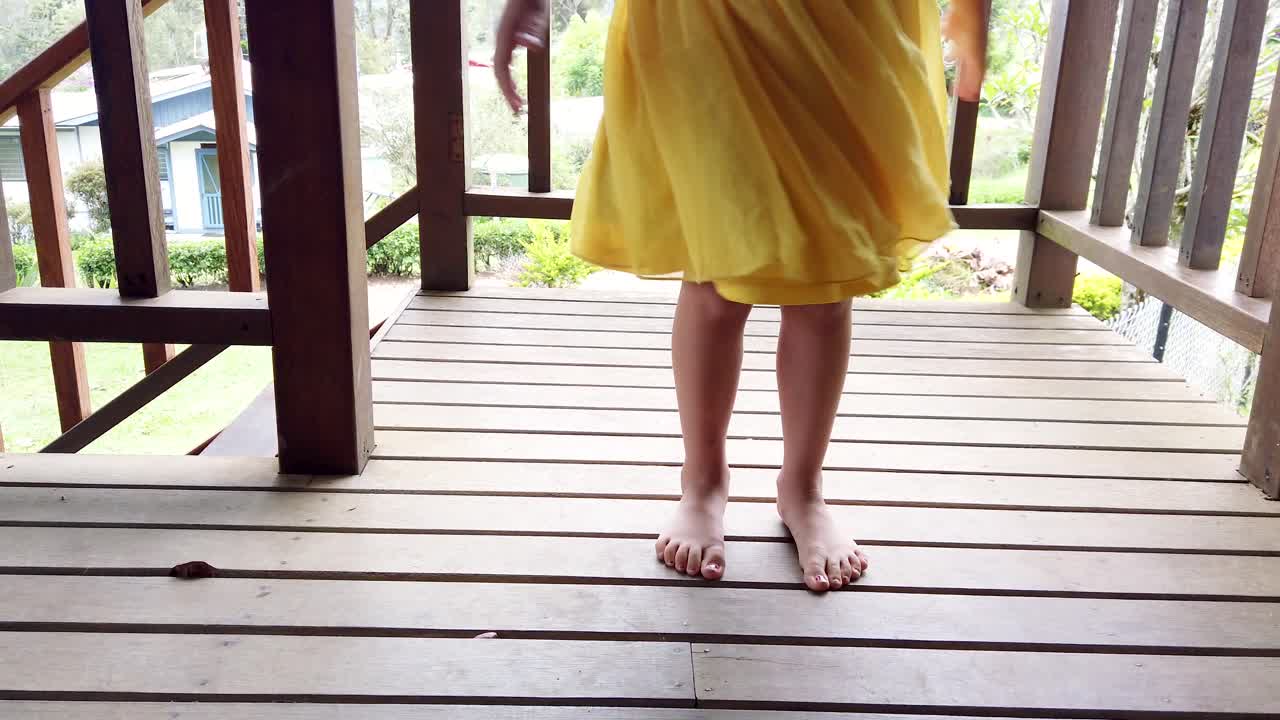 niña despreocupada y juguetona girando con un vestido amarillo en la veranda