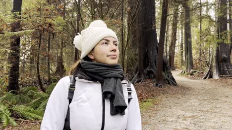 Close-up-young-woman-with-scarf-and-hat-looking-up-enjoying-cold-day-in-the-forest