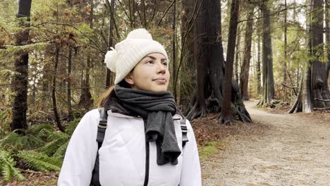 cerca de una mujer joven con bufanda y sombrero mirando hacia arriba disfrutando de un día frío en el bosque