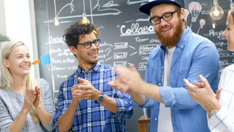 un equipo diverso de desarrolladores creativos aplaudiendo, celebran un año exitoso. jóvenes felices vestidos con estilo en el ambiente de oficina de moda.
