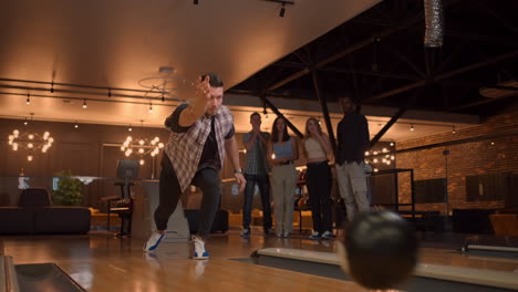 Multi-ethnic-Group-of-friends-in-a-bowling-club-Caucasian-man-throws-a-ball-and-knocks-out-a-strike