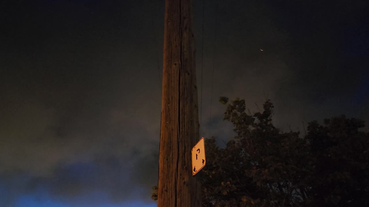 una toma de dolly de cerca mirando hacia un alto pilar de electricidad de madera, el cielo lleno de humo oscuro de un incendio forestal cercano, el lago kirkland, canadá