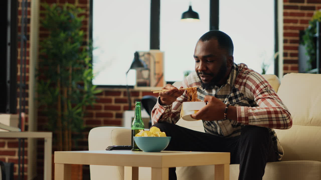 Happy guy eating noodles with chopsticks at home