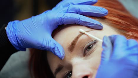 a beauty master completes the procedure of tattooing eyebrows and cleans the client's eyebrows with a cotton swab in a beauty salon. close-up