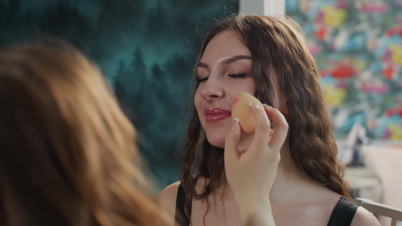 Caucasian Model Smiling While Makeup Sponge Blends Contour And Highlight, Floral Backdrop, Playful Expression, Studio Prep Atmosphere, Friendly Artist Touch And Camera Ready Look