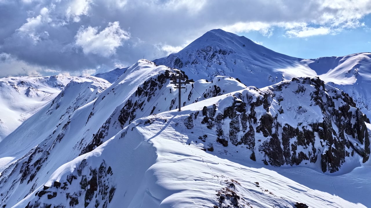 Aerial view of a dramatic snow-covered alpine ridge with rugged peaks and deep winter light, capturing remote mountain wilderness, sharp relief, and high-altitude adventure scenery.