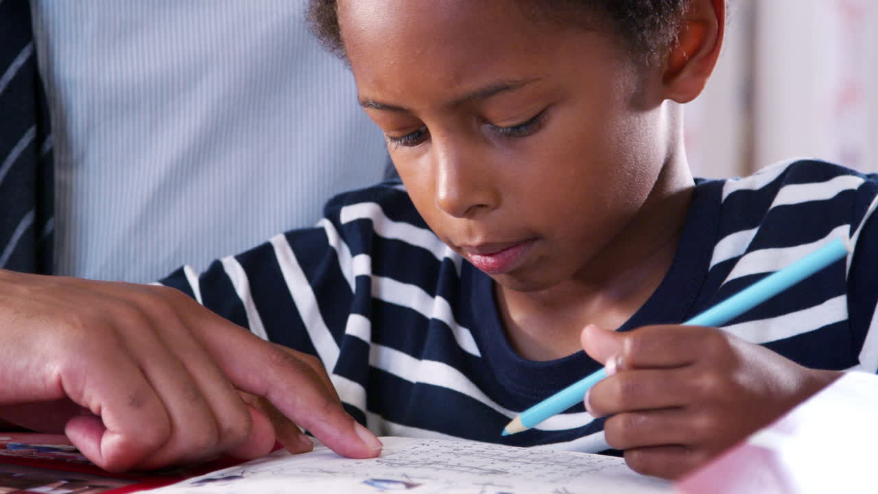 Close Up Of Father Helping Son With Homework In Bedroom At Home