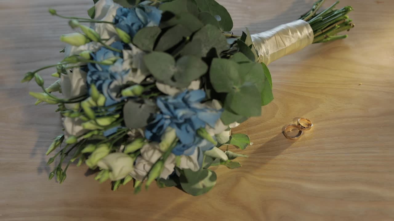 Fedi nuziali giacciono vicino a un bellissimo bouquet da sposa su un tavolo di legno.