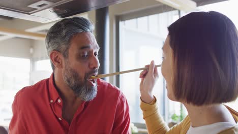 pareja feliz y diversa cocinando y comiendo juntos, probando comida en la cocina