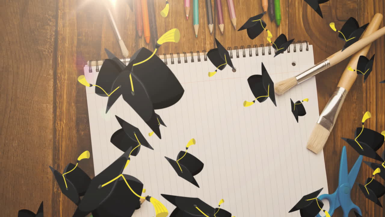 Graduation caps animation over open notebook with pencils and paintbrushes