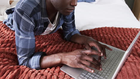 african american man using laptop on bed, focusing on work at home