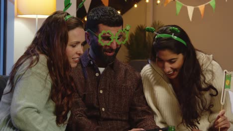 Group-Of-Friends-Dressing-Up-At-Home-Or-In-Bar-Celebrating-At-St-Patrick's-Day-Party-Looking-At-Photos-On-Phone-1