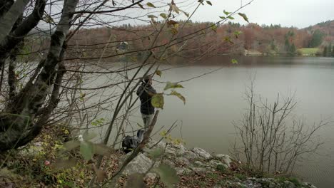 a man getting a tripod out of his backpack to organise the tripod on a rock ledge with a large lake in the background