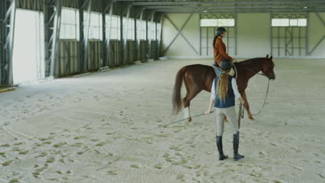 horse riding lesson in an indoor equestrian arena