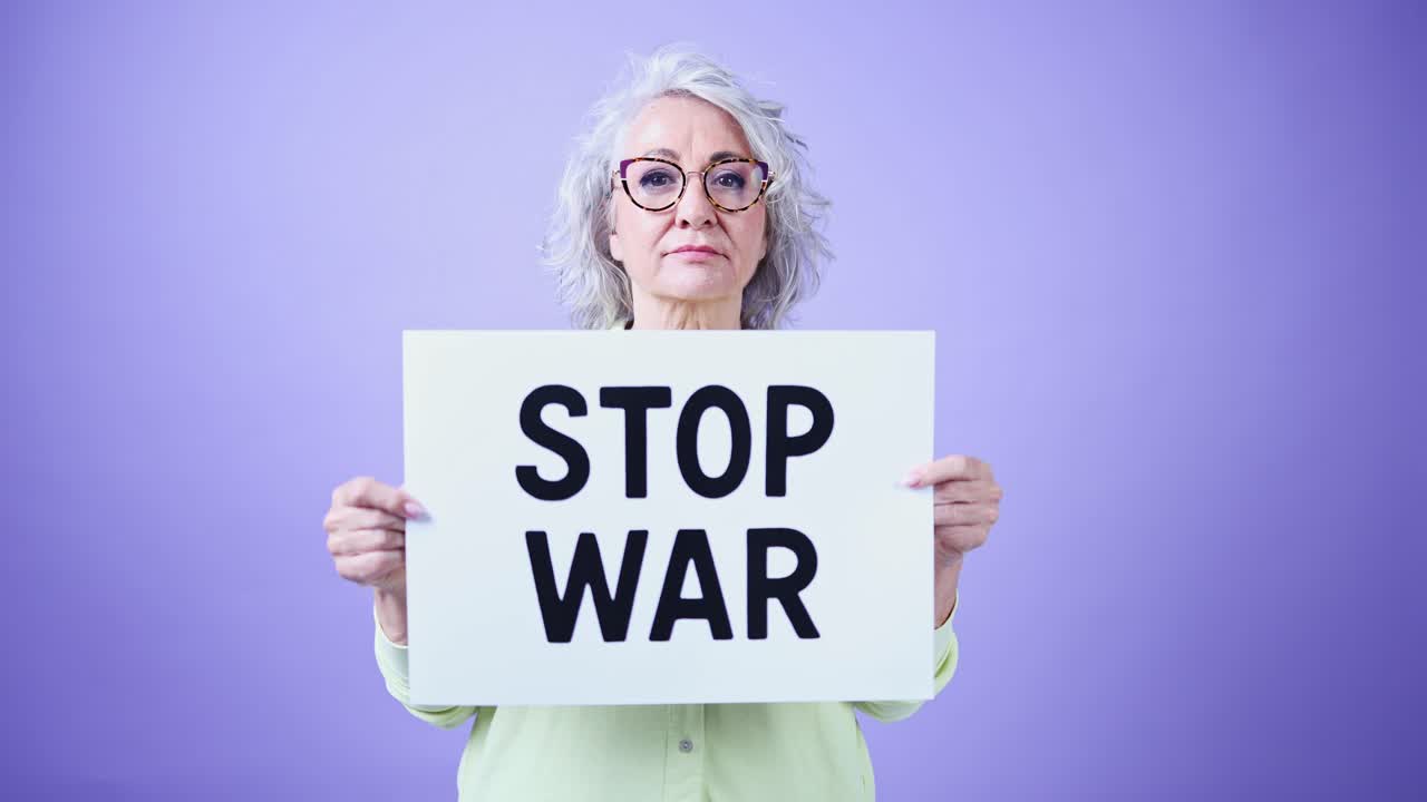 Donna anziana che tiene un cartello con scritto 'Stop alla guerra' su sfondo viola