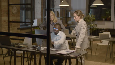 american businessman showing something on computer to his two female colleagues and discussing together in the office