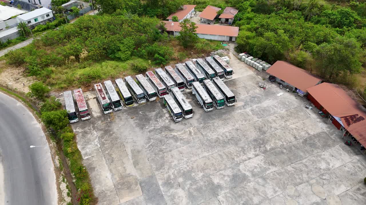 las imágenes de drones capturan un estacionamiento de autobuses desierto en phuket, tailandia, mostrando vehículos oxidados y alrededores cubiertos de vegetación a la luz del día.