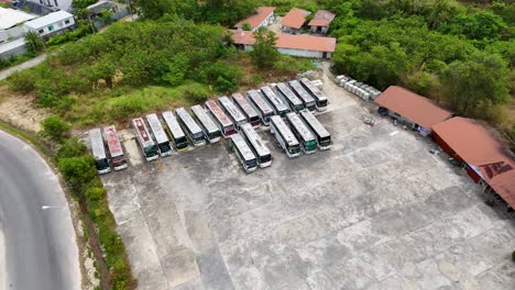 drone footage captures a deserted bus lot in phuket, thailand, showcasing rusting vehicles and overgrown surroundings in bright daylight