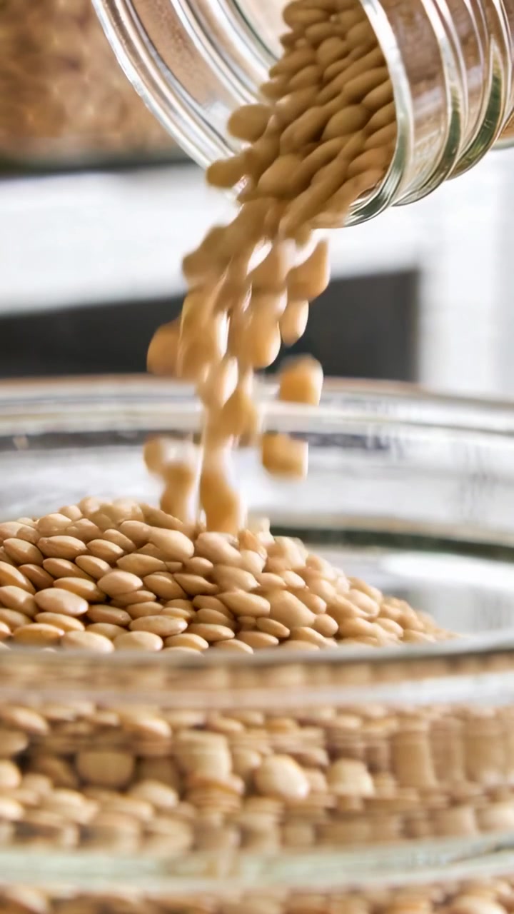 Video verticale: Vaso di vetro che si inclina versando lenticchie in ciotole per mescolare sul bancone, per cucinare