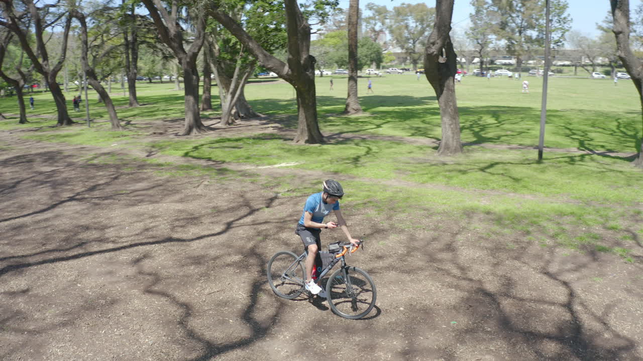 Man Standing with Bike on Park Road and Using Phone