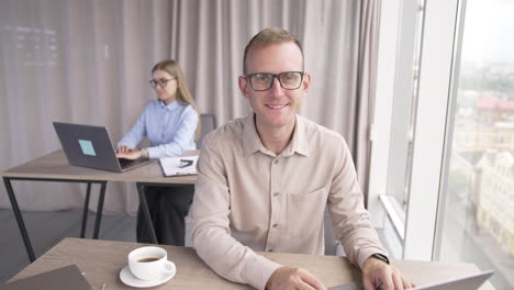 young mid-aged teammates working in the office sitting in front of laptops. portrait of a male employee wearing glasses close up.