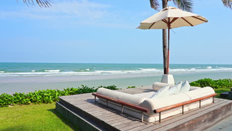 Group-lounge-with-beach-Parasol-and-comfortable-bed-on-a-wooden-platform-near-the-sea-under-a-coconut-palm-tree