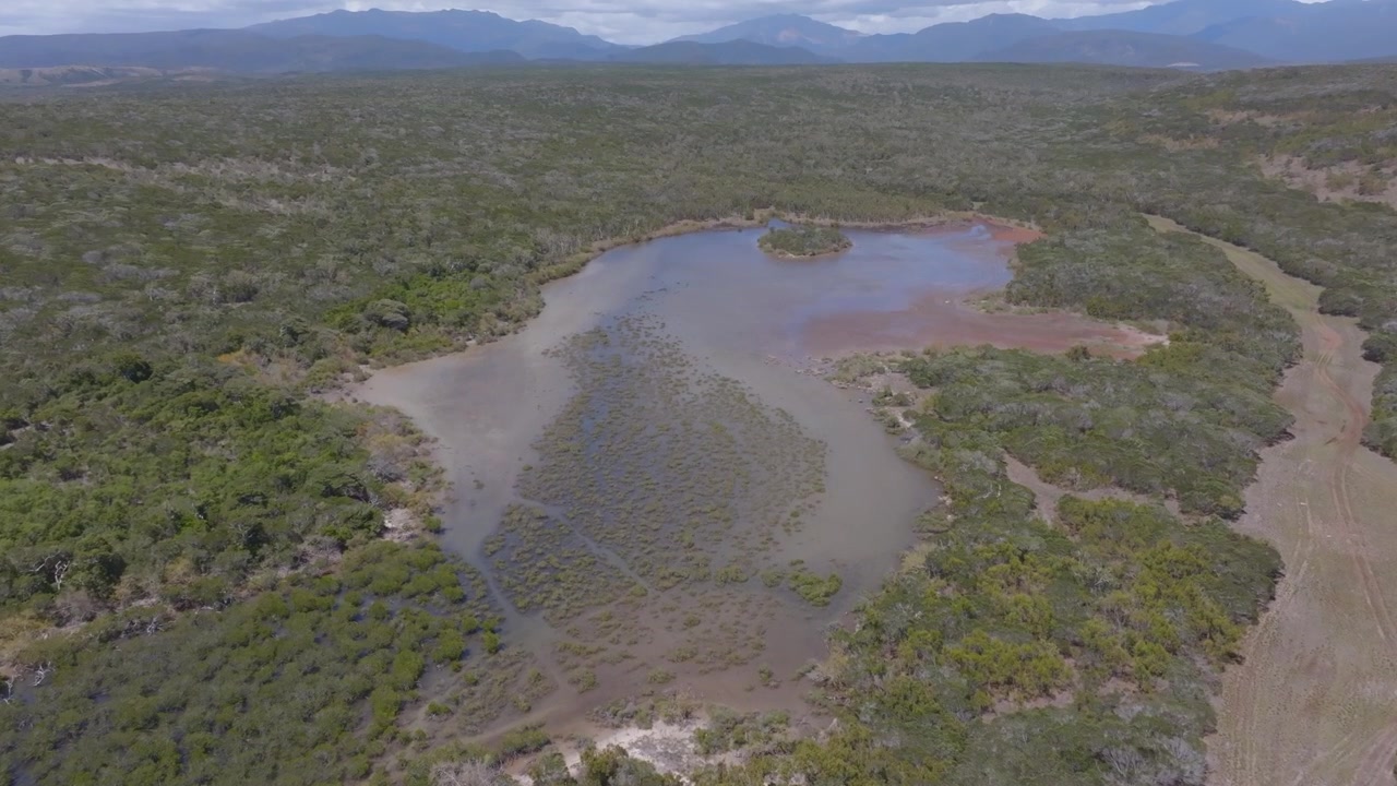 Deslize de drone para a frente em direção a um lago tropical isolado cercado por vegetação densa, com montanhas distantes adicionando escala e uma sensação de natureza selvagem remota, ideal para narrativas de natureza e viagens