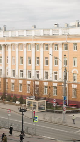 vista cercana de una concurrida intersección de la ciudad con un edificio amarillo ornamentado, coches en movimiento, y en un día nublado señales de tráfico, luces de la calle y transporte público