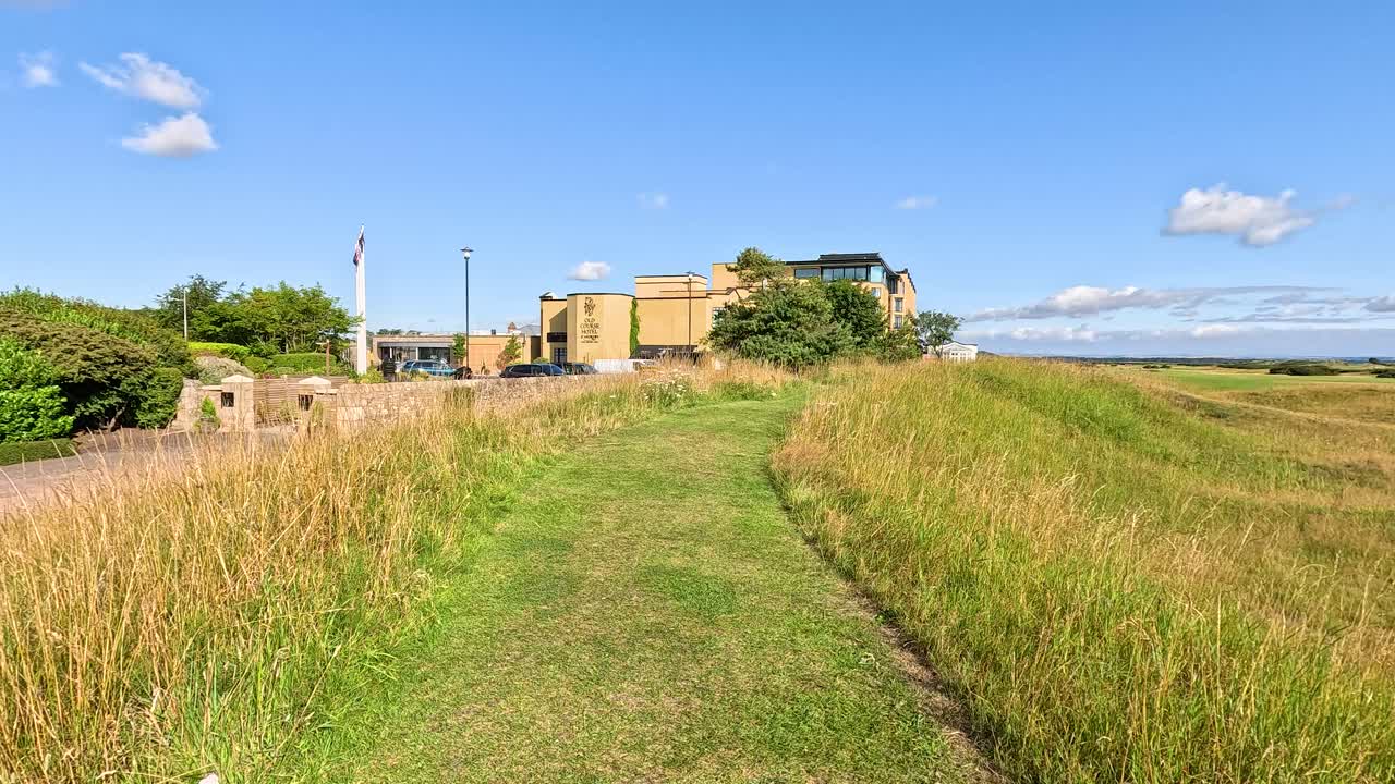 Forward-moving camera along grassy path toward iconic hotel, bright daylight, clear blue sky