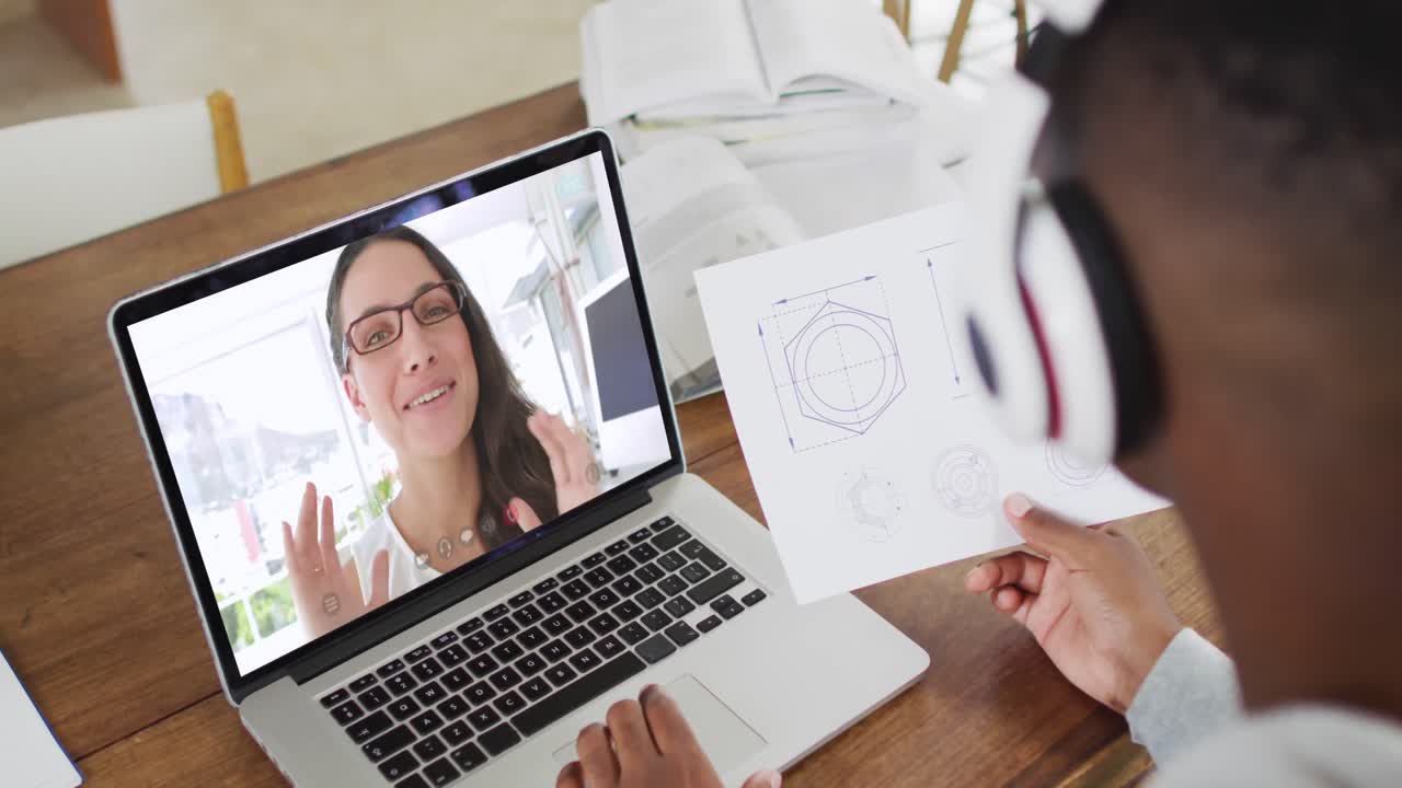 estudiante universitario afroamericano que sostiene notas mientras hace una videollamada en una computadora portátil en casa