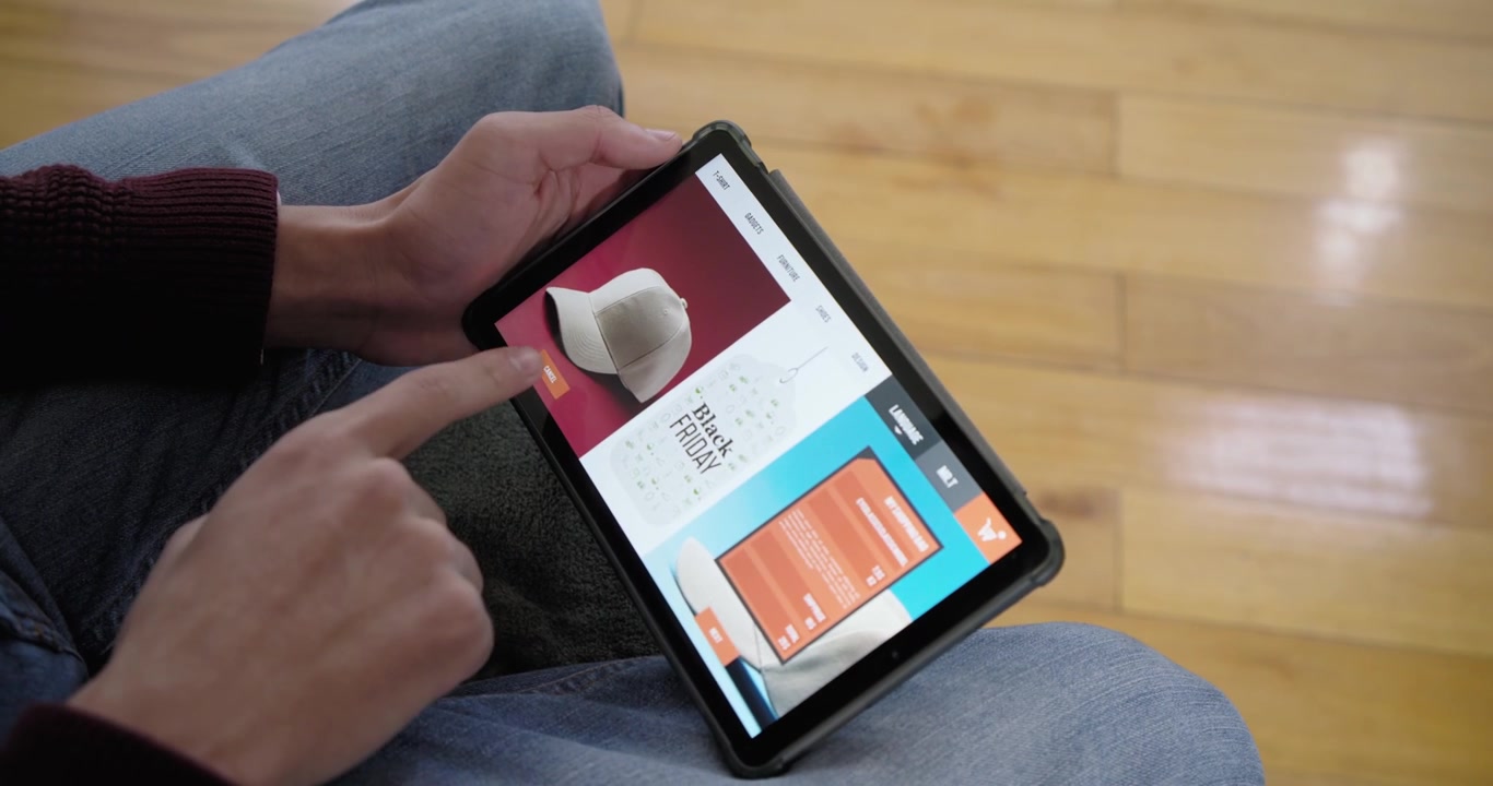African American man holding tablet, tapping swiping browsing Black Friday white hat card on lap