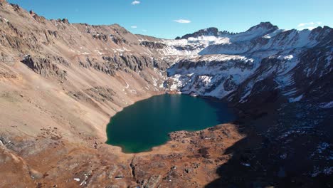 Drone-shot-of-a-large-mountain-lake-with-snowy-peaks-and-a-sunny-day