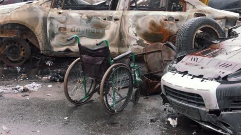 rain falling on wheelchair amid wrecked, charred vehicles in ukraine after devastating russian attacks. - wide shot